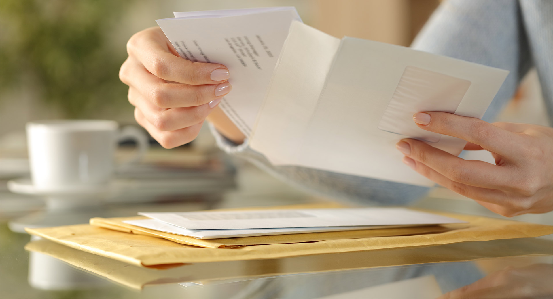 A close-up of a person sat at a table pulling a letter out of an envelope